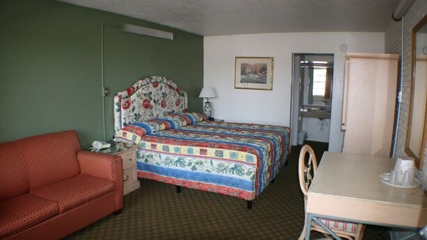 A room with a bed, a desk, a chair, a red sofa, and a door. - Budget Inn (Charlotte)