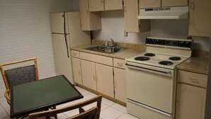 A compact kitchen with a stove, sink, and cabinets. There is a small table with chairs. - Budget Inn (Charlotte)