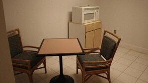 A small room with a table and two chairs, a microwave on top of a cabinet, and a tiled floor. - Budget Inn (Charlotte)