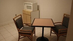 A small room with a wooden cabinet, a microwave on top, two chairs, and a square table. - Budget Inn (Charlotte)