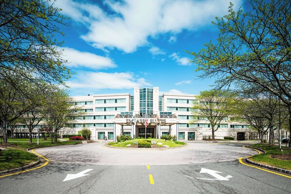 A large, modern building with a central entrance, surrounded by a well-maintained lawn and trees. - Embassy Suites by Hilton Parsippany (Parsippany)