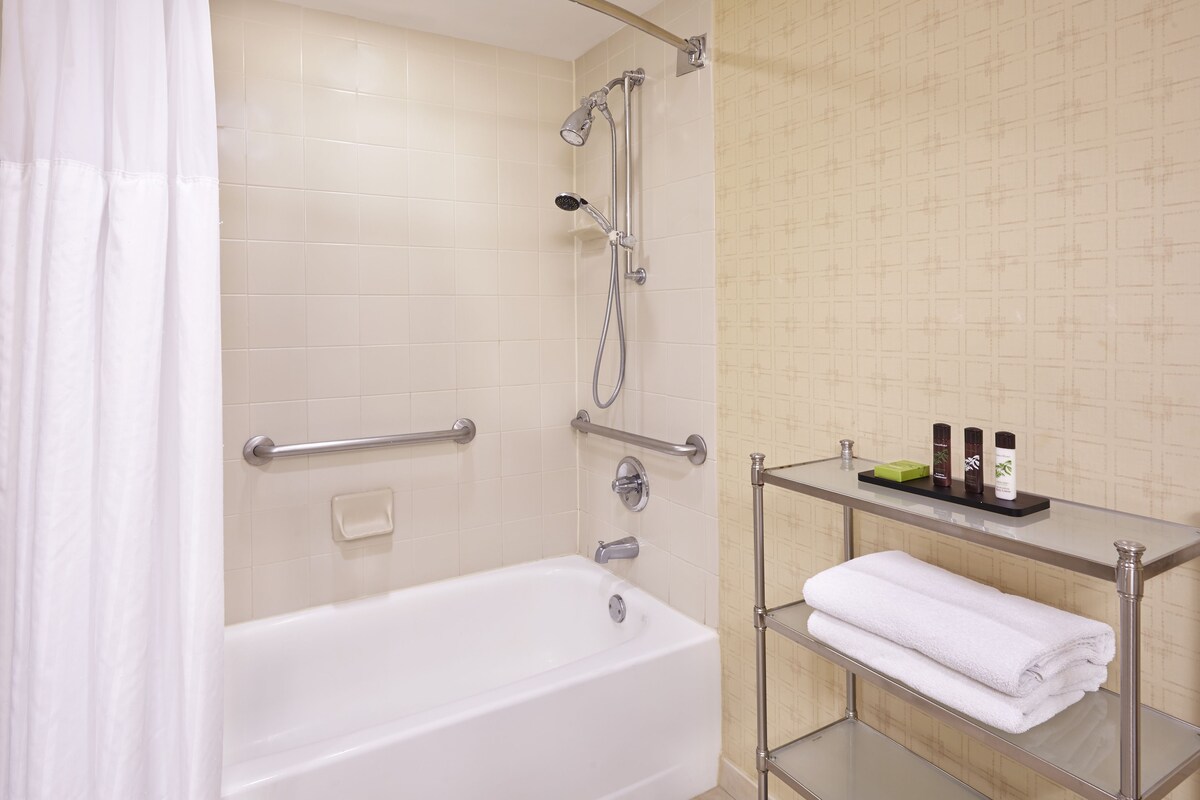 Ein Badezimmer mit einer Badewanne, einer Dusche, einer Glasablage für Toilettenartikel und einem Handtuchhalter.