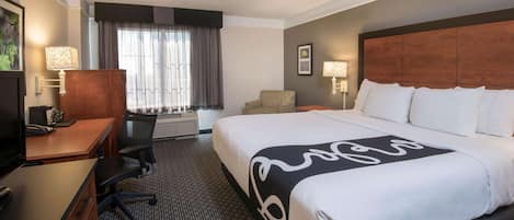 A hotel room with a large bed, a desk with a chair, a television, and a window with curtains.