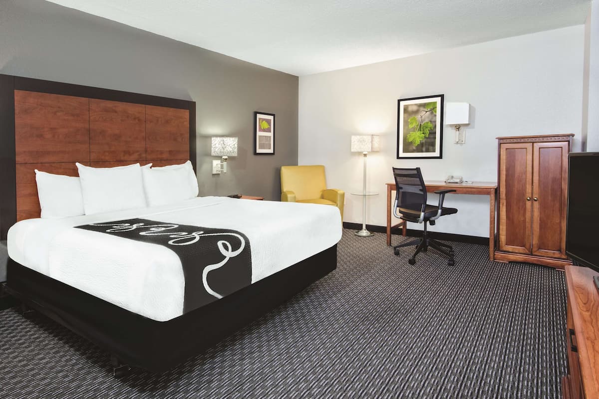 Une chambre d’hôtel avec un grand lit, un bureau avec une chaise, une lampe et une armoire.