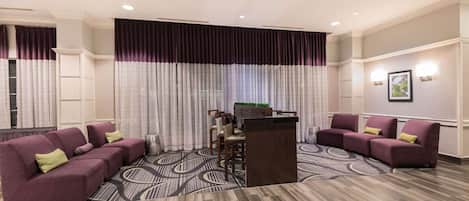 A hotel lobby with a reception desk, purple sofas, and a patterned carpet.