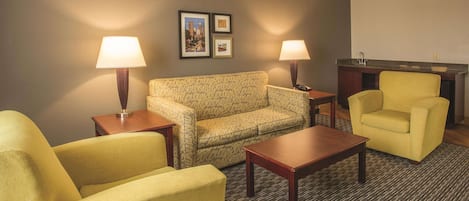 Una habitación de hotel con un sofá estampado, un sillón amarillo, una mesa de centro de madera y dos lámparas.