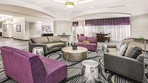 A spacious hotel lobby with a curved ceiling, multiple seating areas, and a large window with purple curtains.