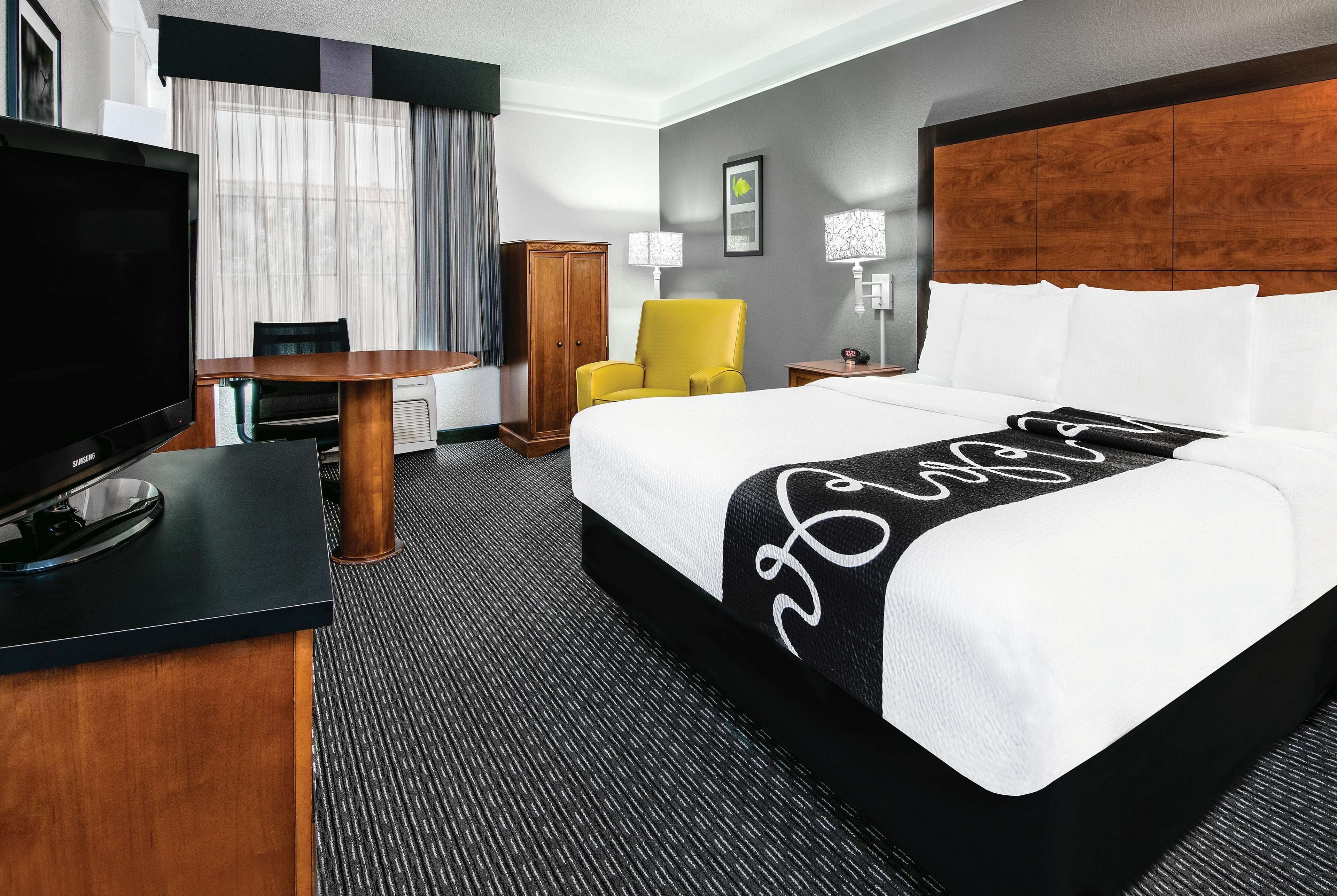 A hotel room with a bed, a TV, a desk, a chair, and a lamp.