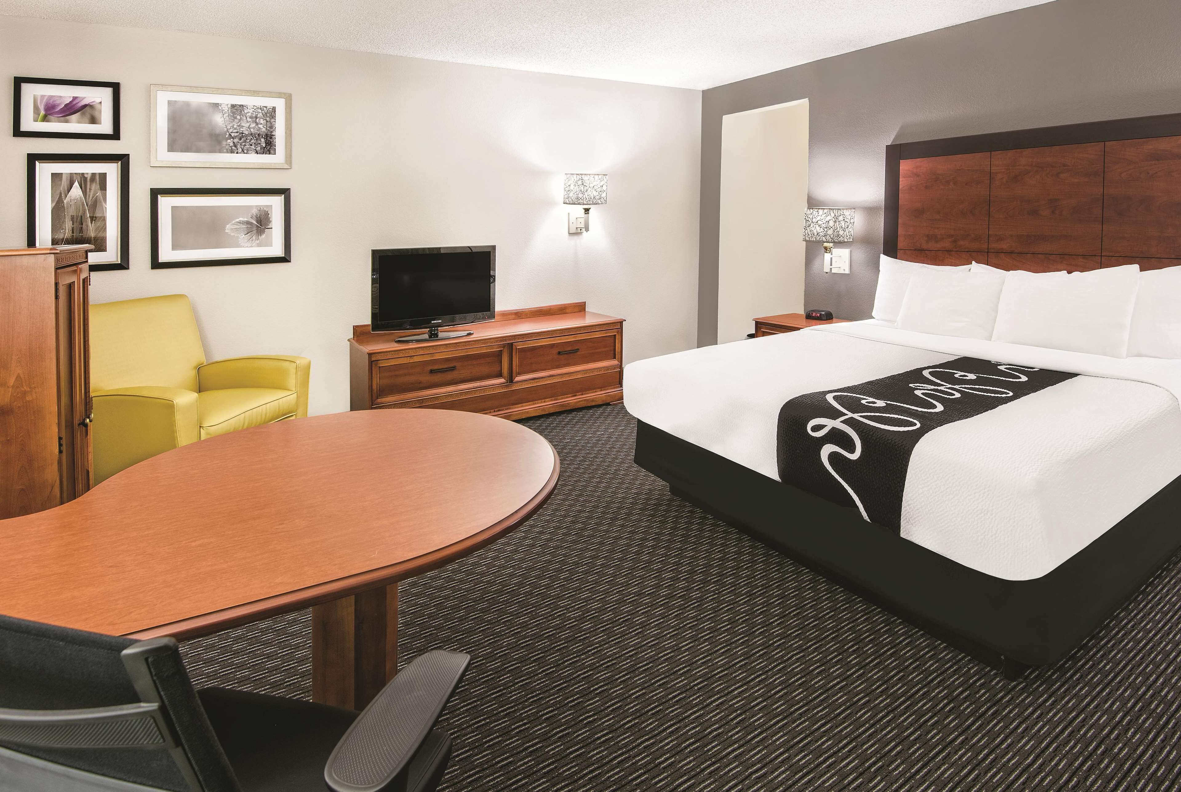 A hotel room with a bed, a desk, a chair, a television, and framed pictures on the wall.