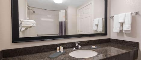 A bathroom with a large mirror, a sink, and a shower.