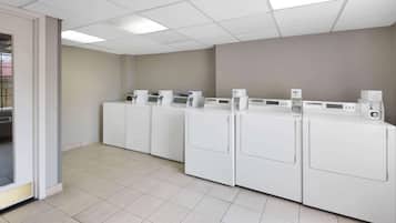 A laundry facility with multiple washing machines and dryers, a tiled floor, and a plain wall.