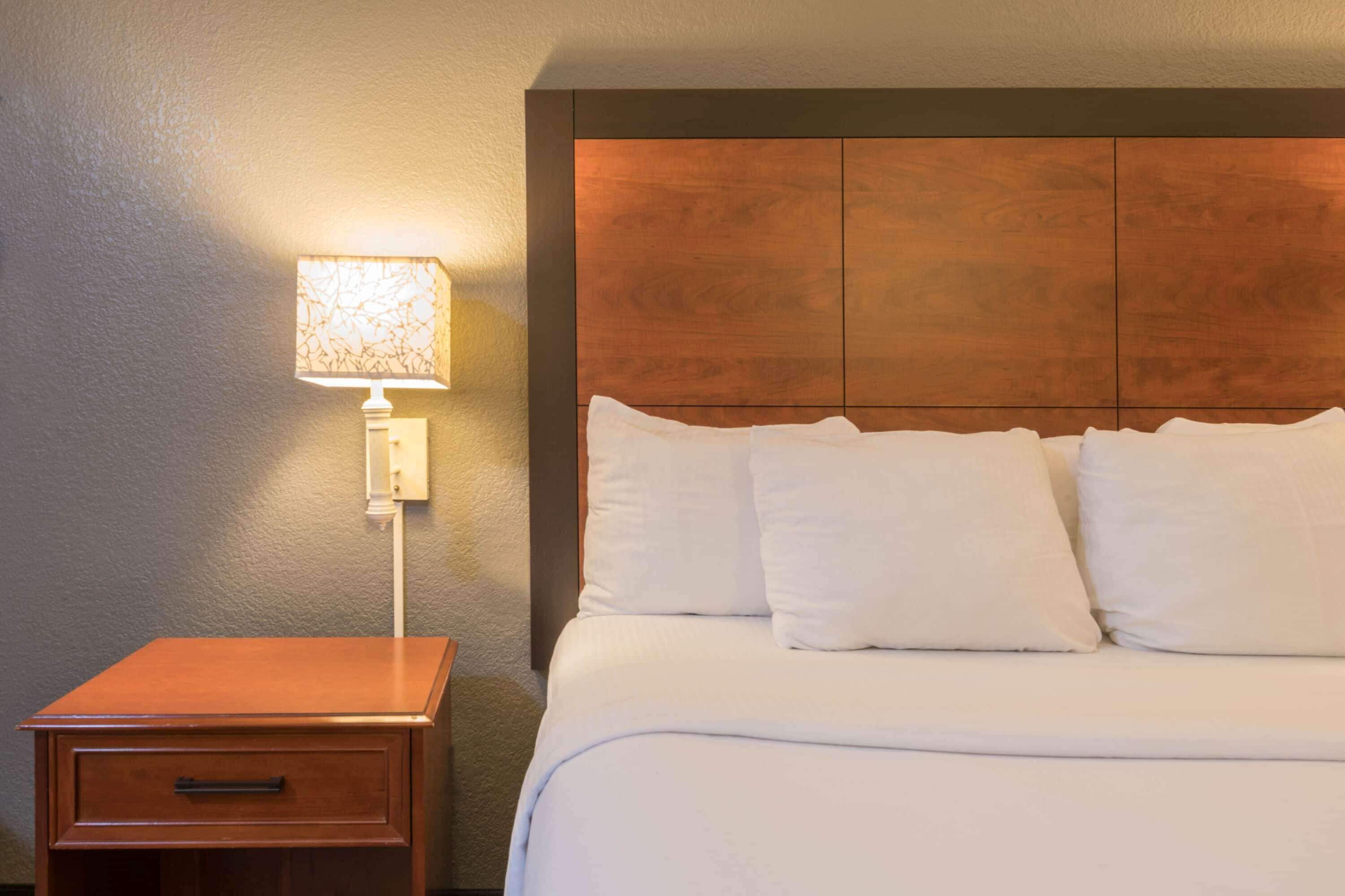 A hotel room with a wooden headboard, a bedside table with a lamp, and a neatly made bed.