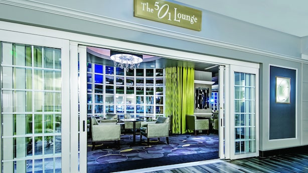 A hotel lobby with a sign reading "The 501 Lounge," featuring a modern design with a chandelier, seating area, and a view into the lounge.