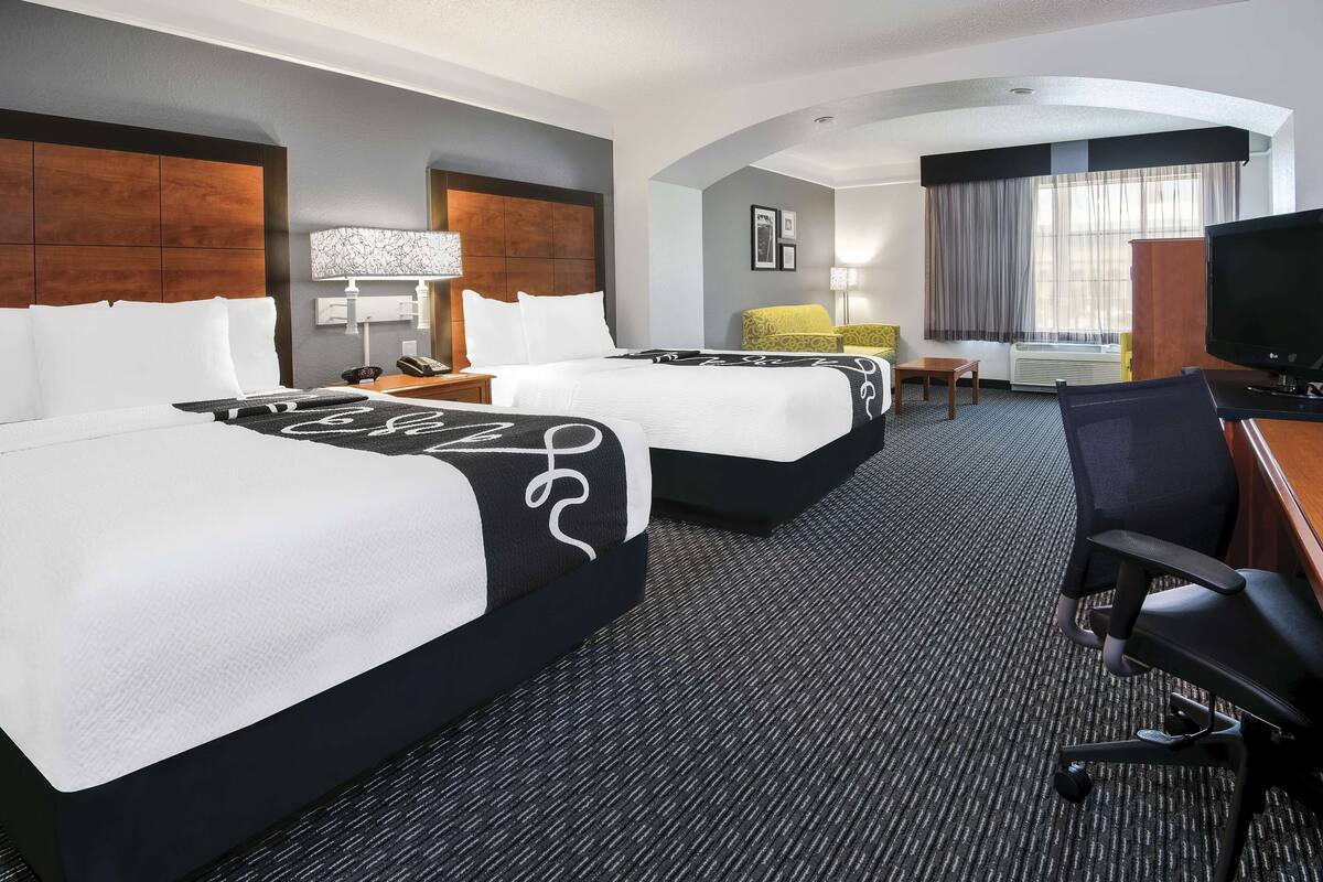 Une chambre d’hôtel avec deux lits, un bureau avec une chaise, une télévision et une fenêtre avec des rideaux.