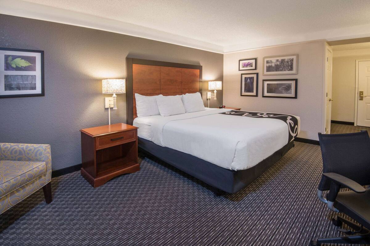 Une chambre d’hôtel avec un grand lit, une table de chevet en bois, un bureau, une chaise et des tableaux encadrés au mur.