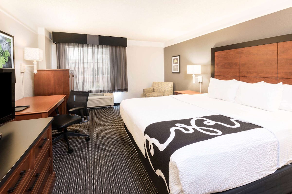Une chambre d’hôtel comprenant un lit, un bureau avec une chaise, une télévision, une fenêtre avec des rideaux et une lampe fixée au mur.
