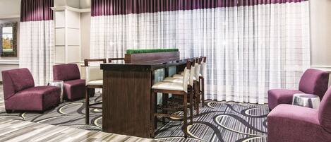 A hotel lobby with purple chairs, a bar area, and a patterned floor.
