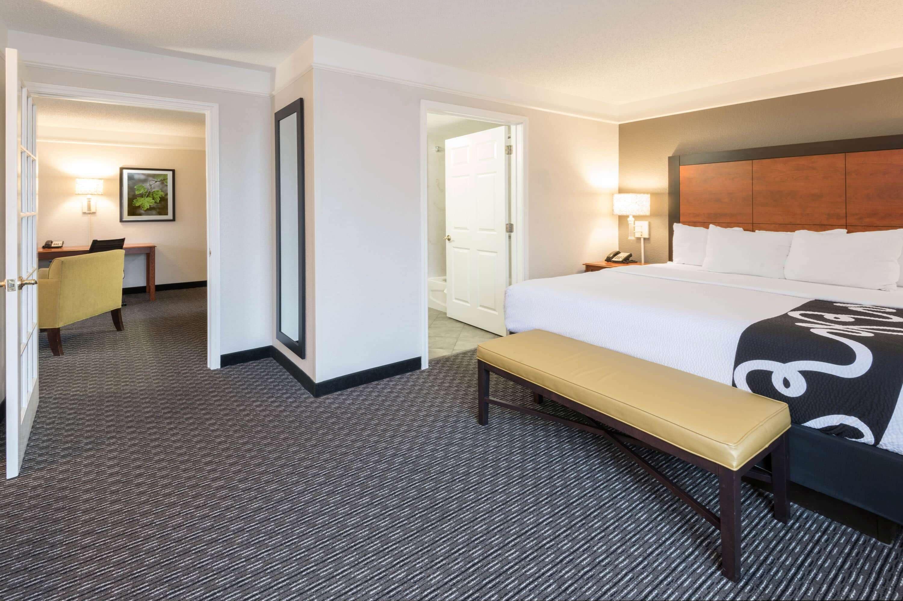 A hotel room with a large bed, a bench, a desk, and a chair.