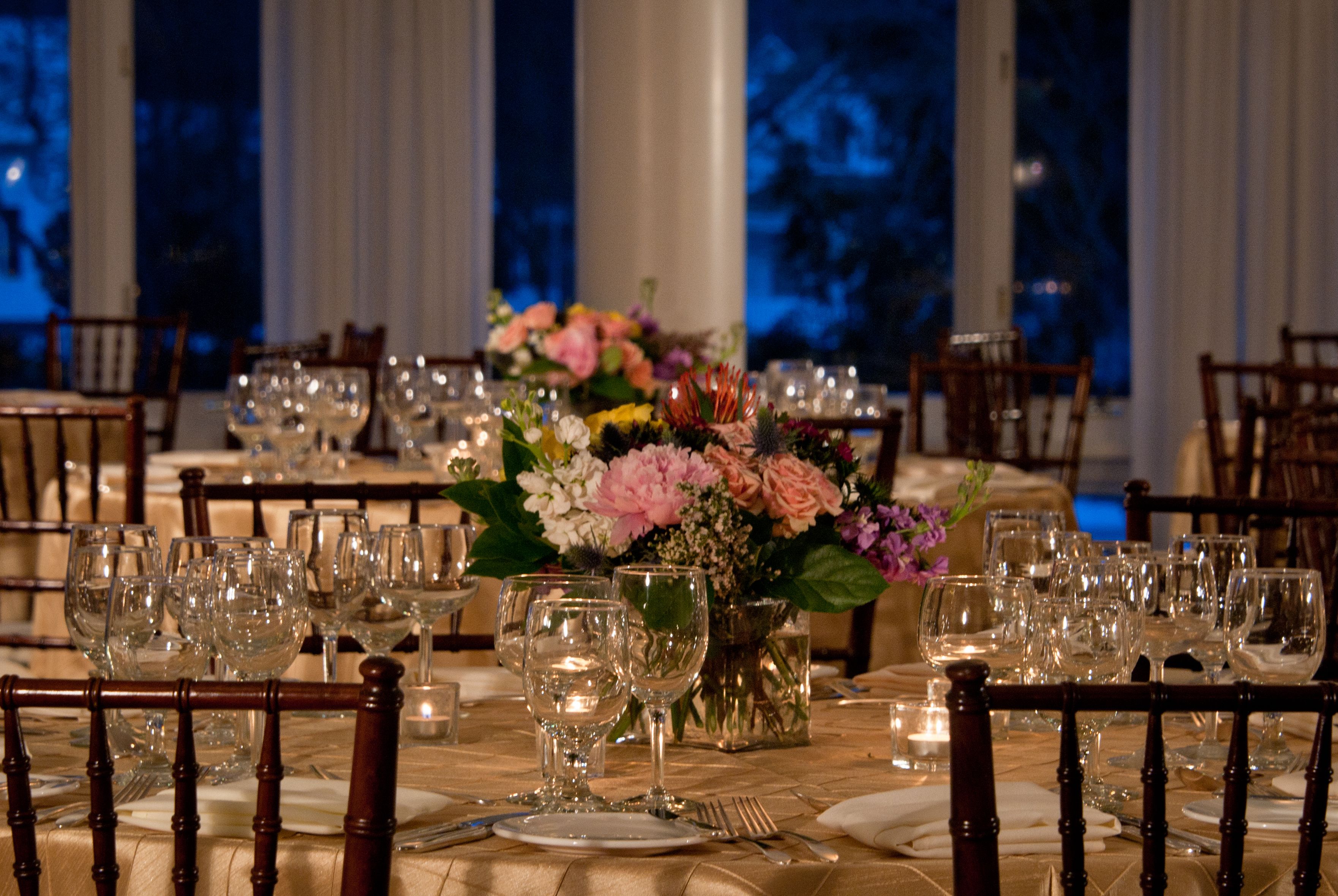 Une salle à manger élégante, avec des tables dressées pour accueillir plusieurs convives, comprenant de la verrerie, de la vaisselle et un centre de table composé de fleurs.