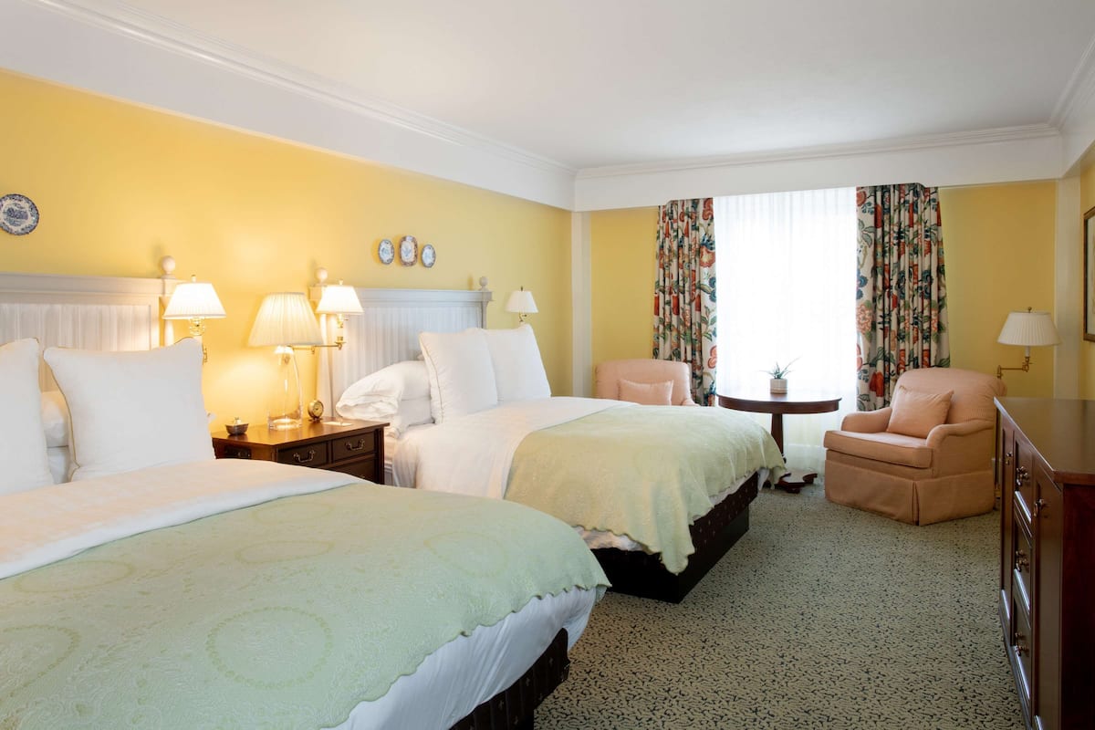 A hotel room with two beds, a chair, a table, and a dresser.