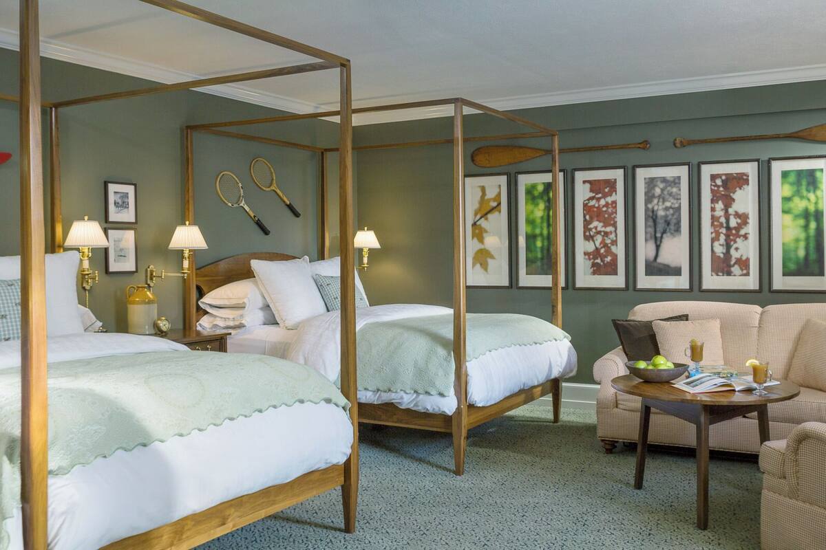 A hotel room with two beds, a sofa, a coffee table, and framed artwork on the walls.
