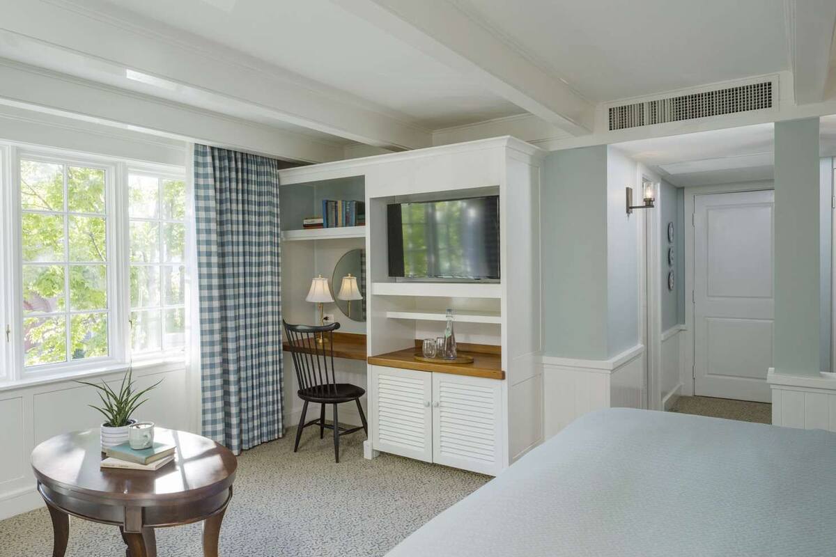 A bedroom with a bed, a desk with a TV, a chair, and a window with curtains.