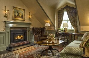 A cozy room with a fireplace, a green sofa, a dining table with a vase of flowers, and a large window with curtains.