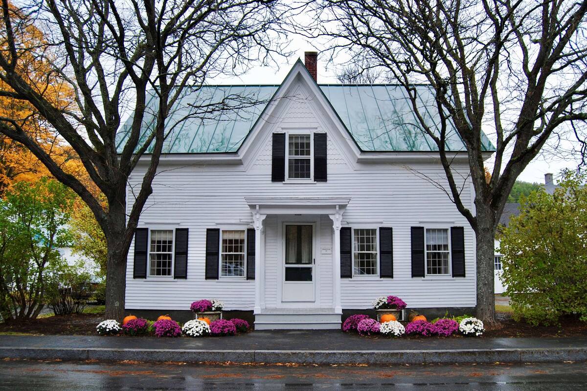 A white house with black shutters, a central door, and a gabled roof.