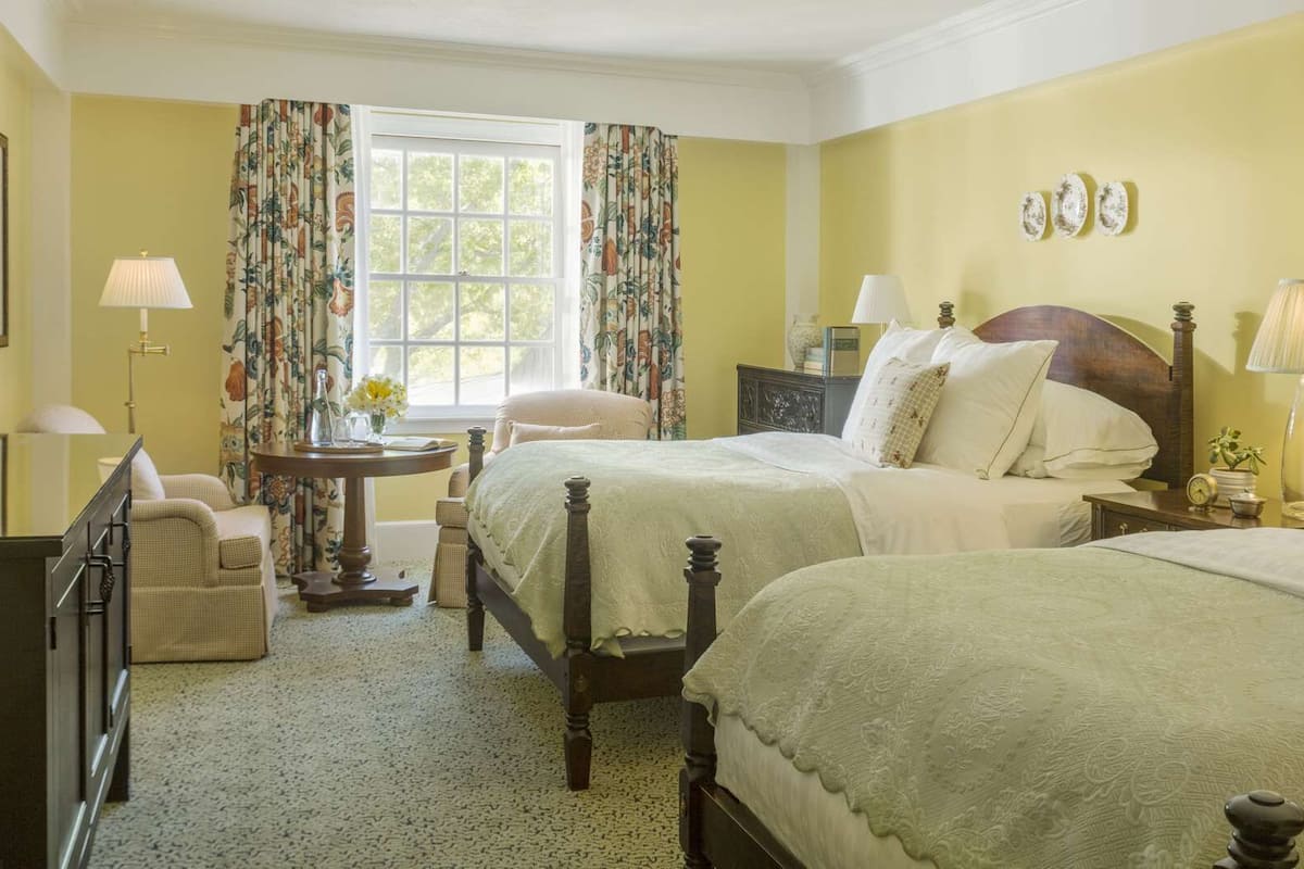 A bedroom with two beds, a desk, a chair, and a window with curtains.