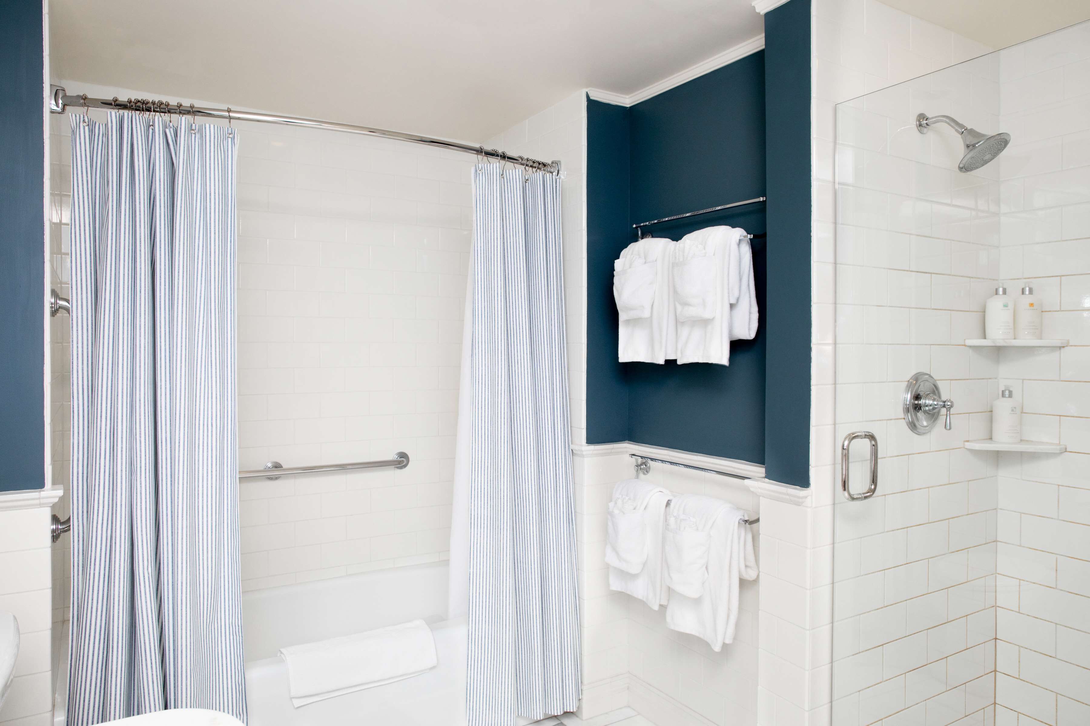 A bathroom with a shower, a bathtub, and a towel rack with multiple towels.
