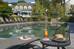 A poolside area with lounge chairs, umbrellas, and a table with a drink and a hat.
