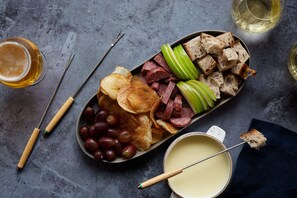 A charcuterie board with various meats, cheeses, and fruits on a slate plate, accompanied by a dipping sauce and a glass of beer.