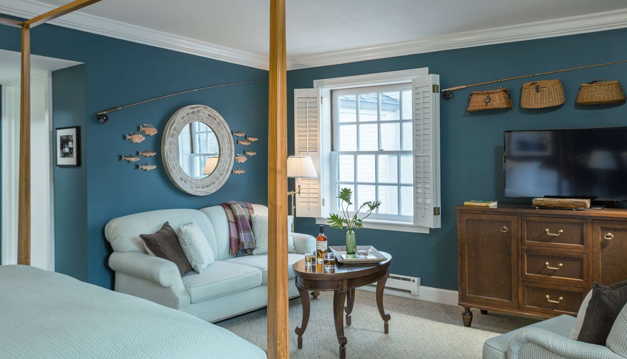 A room with a large window, a television, a round mirror, and a wooden cabinet.