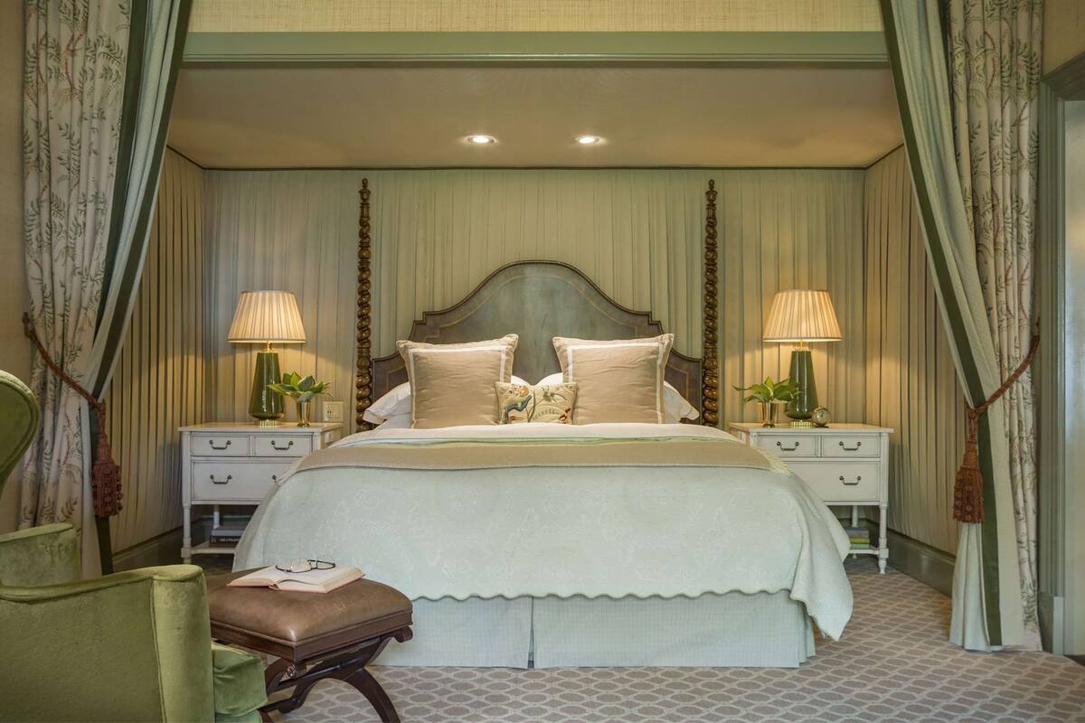 A large bed with a wooden headboard, two bedside tables with lamps, and a bench with a book and glasses.