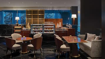 A modern hotel lobby with a central seating area, a dessert display, and a large window with a view.