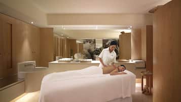 A spa room with a massage table, a bathtub, and a large mirror.