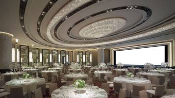 Un salón de banquetes lujoso con varias mesas redondas, cada una con mantel blanco, sillas y centros de mesa florales.