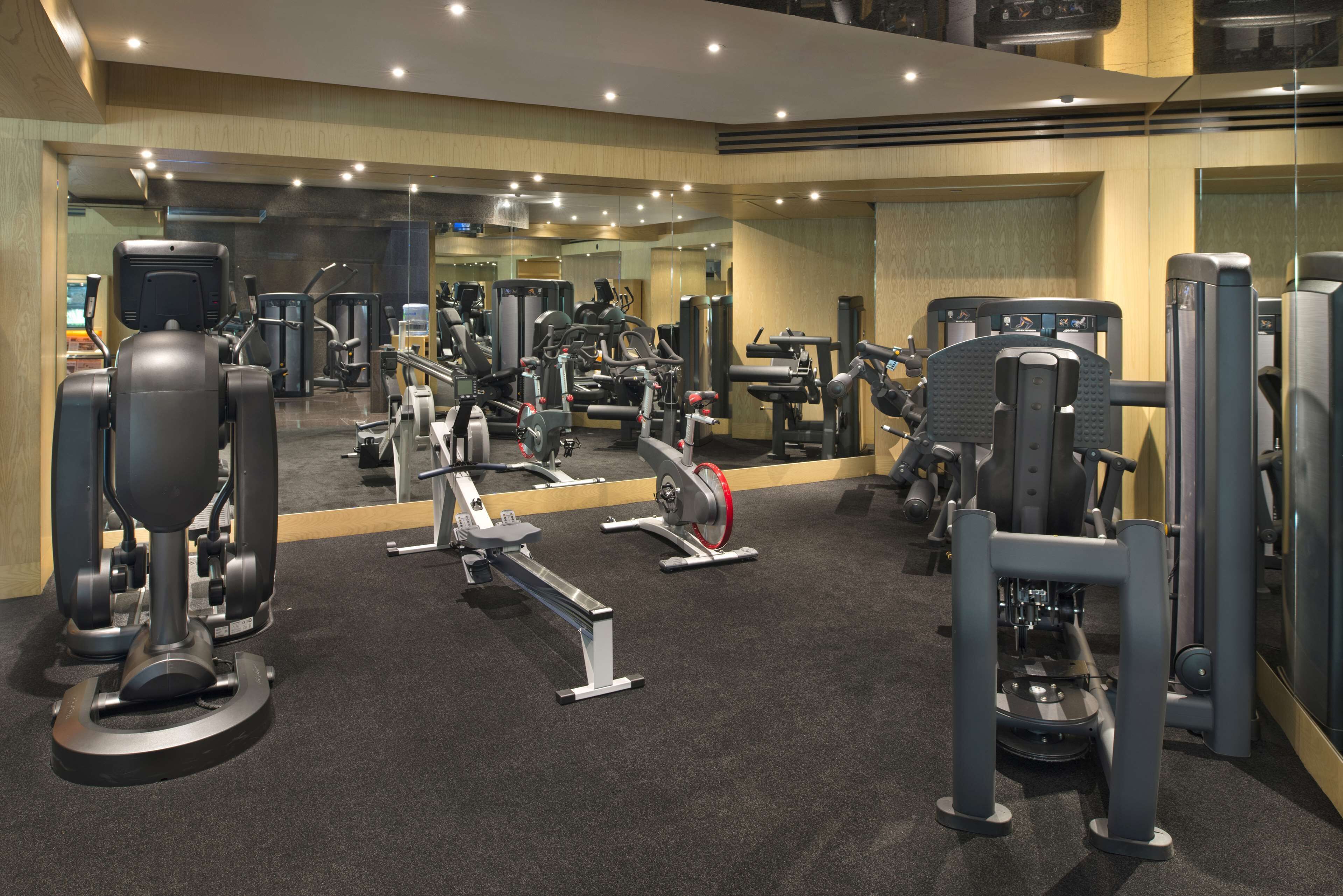 Een fitnessruimte met diverse fitnessapparaten, een spiegelwand en een vloerbedekking.