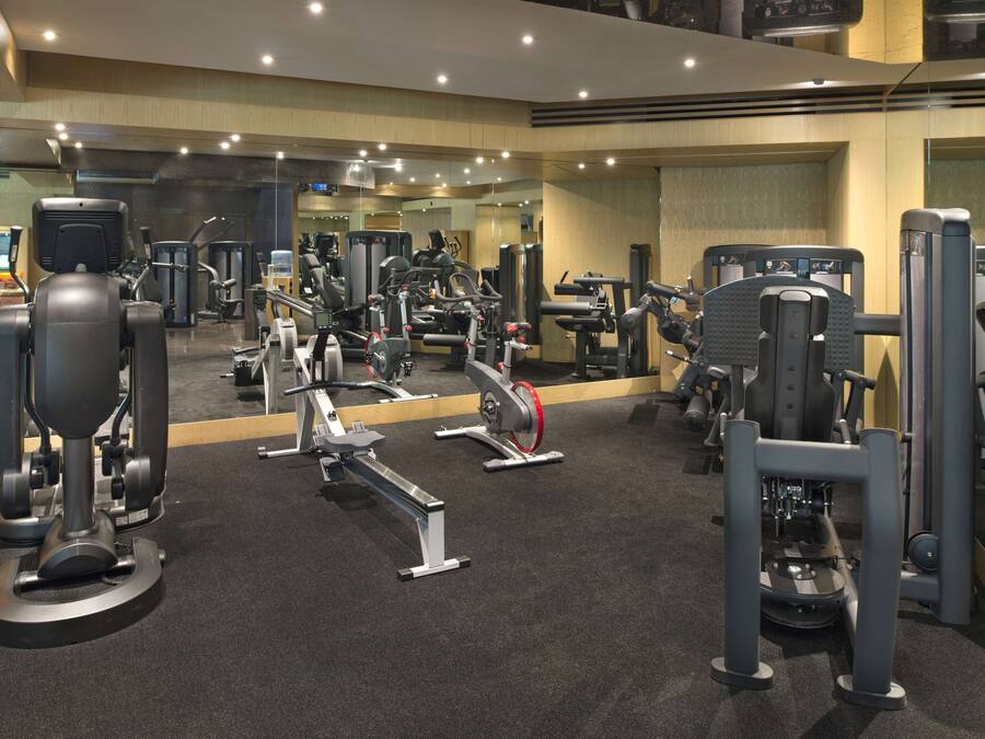 Een fitnessruimte met diverse fitnessapparaten, een spiegelwand en een vloerbedekking.