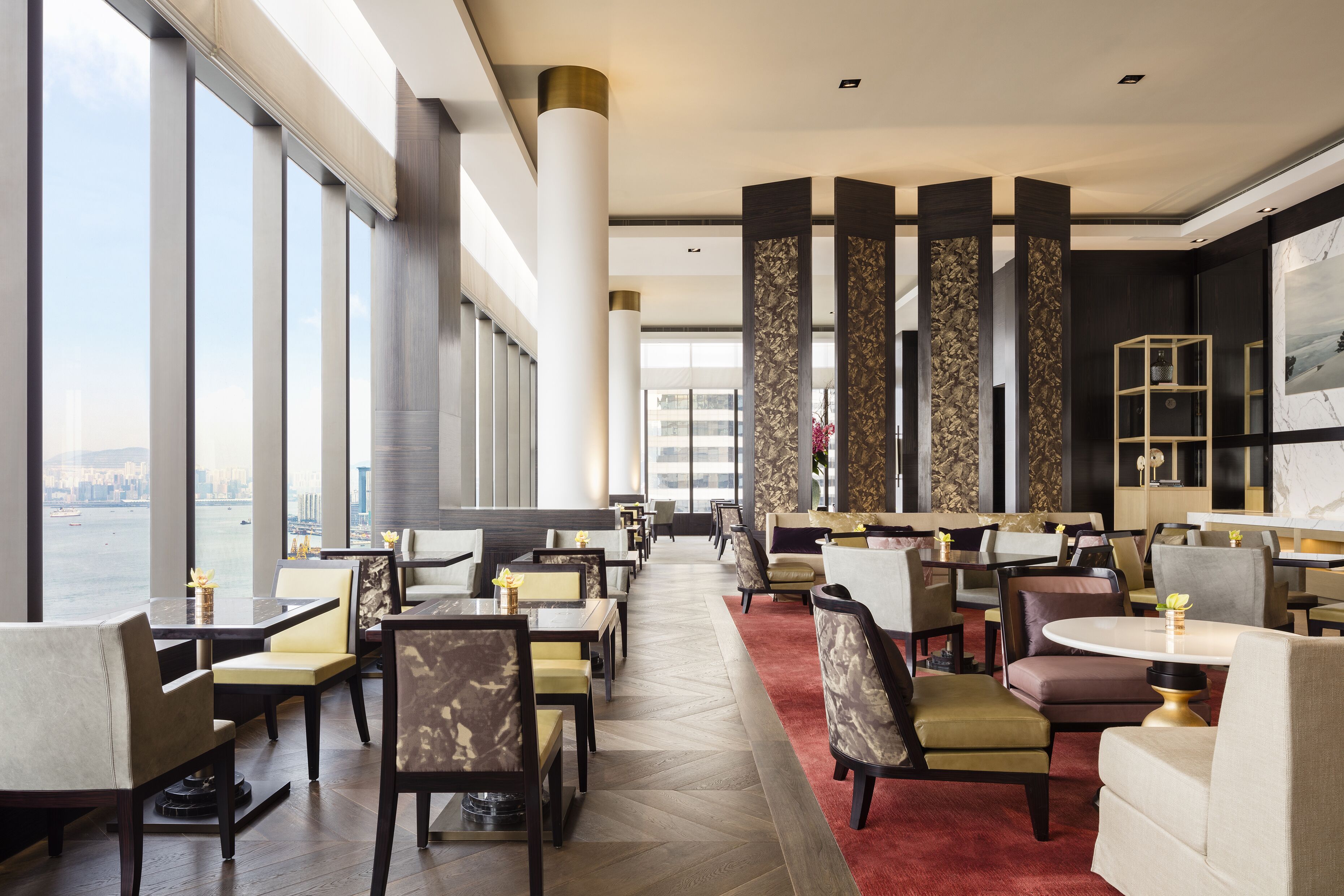 A modern dining area with high ceilings, large windows, and a view of a cityscape.