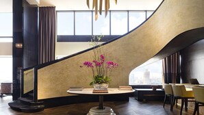 Un intérieur moderne avec un escalier en colimaçon, une table ronde agrémentée d’une plante en pot et une vue sur la ville grâce à de grandes fenêtres.