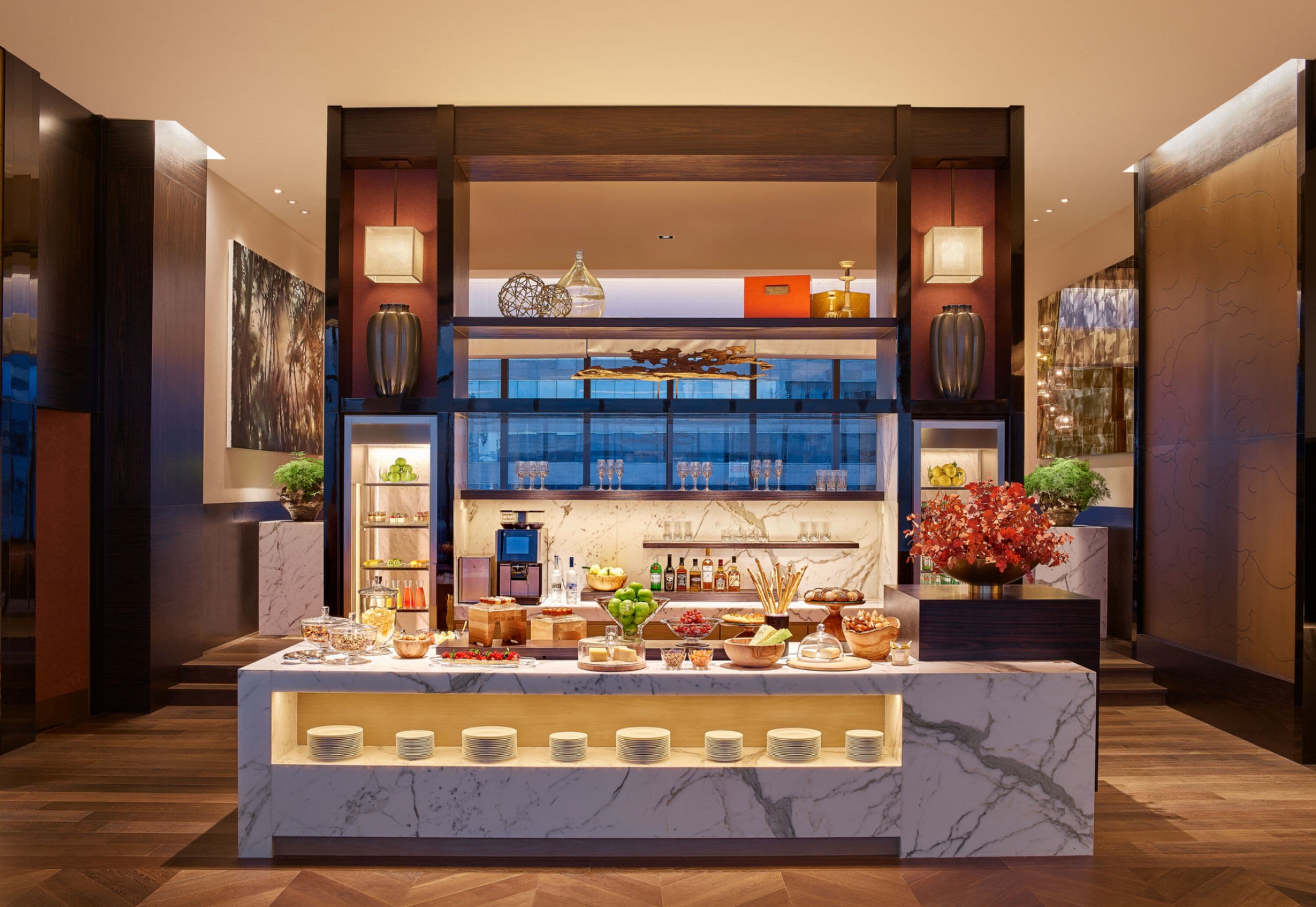 Un aparador de buffet amb una varietat d'aliments i begudes, un taulell de marbre i elements decoratius com vases i plantes.