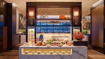 Un aparador de buffet amb una varietat d'aliments i begudes, un taulell de marbre i elements decoratius com vases i plantes.
