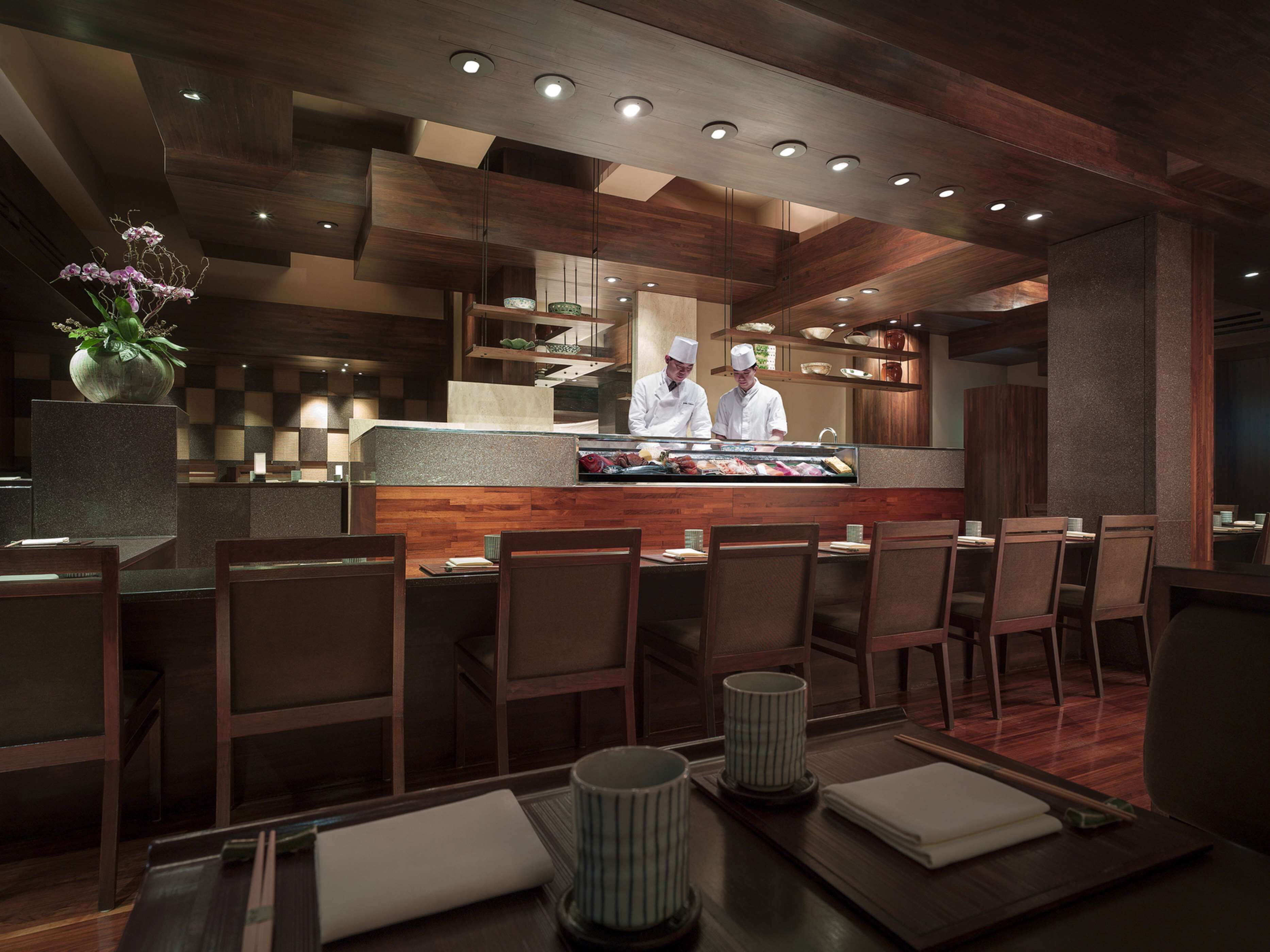 A modern restaurant interior with wooden paneling, a central bar area, and seating for guests.
