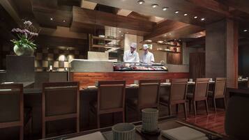 A modern restaurant interior with wooden paneling, a central bar area, and seating for guests.