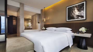 A modern hotel room with a large bed, a bedside table with a vase of flowers, and a framed picture on the wall.