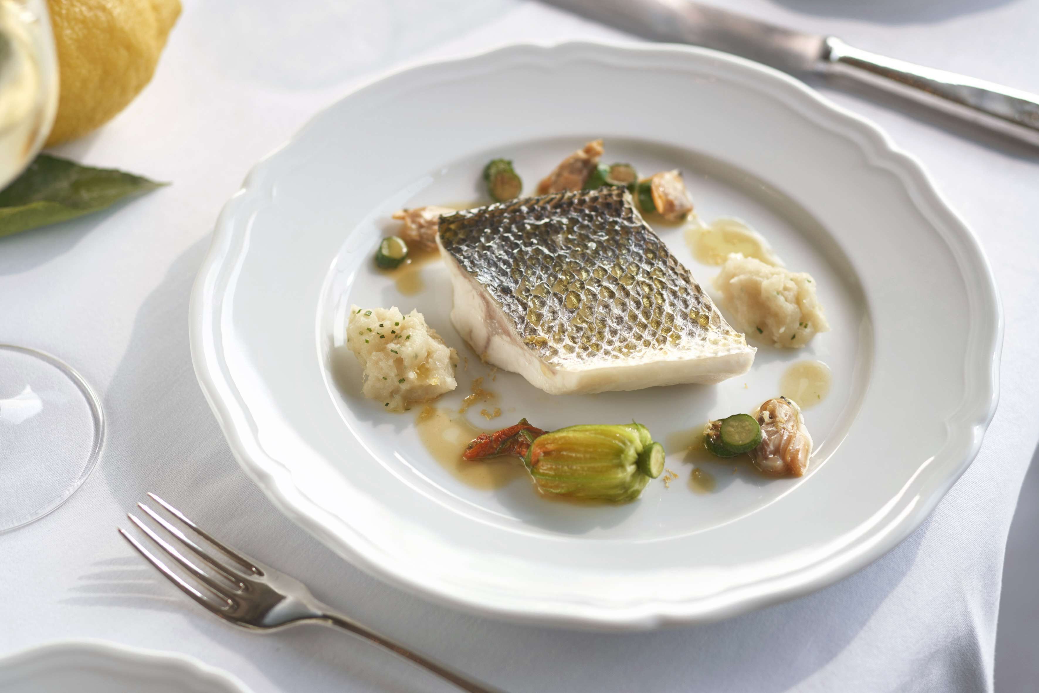 A white plate with a piece of fish, some vegetables, and sauce.