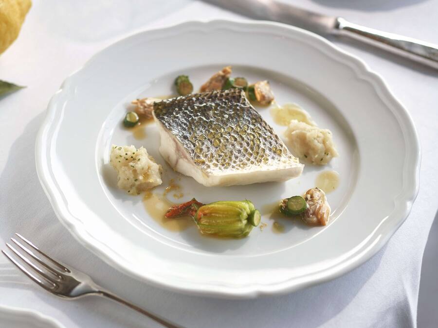 A white plate with a piece of fish, some vegetables, and sauce.