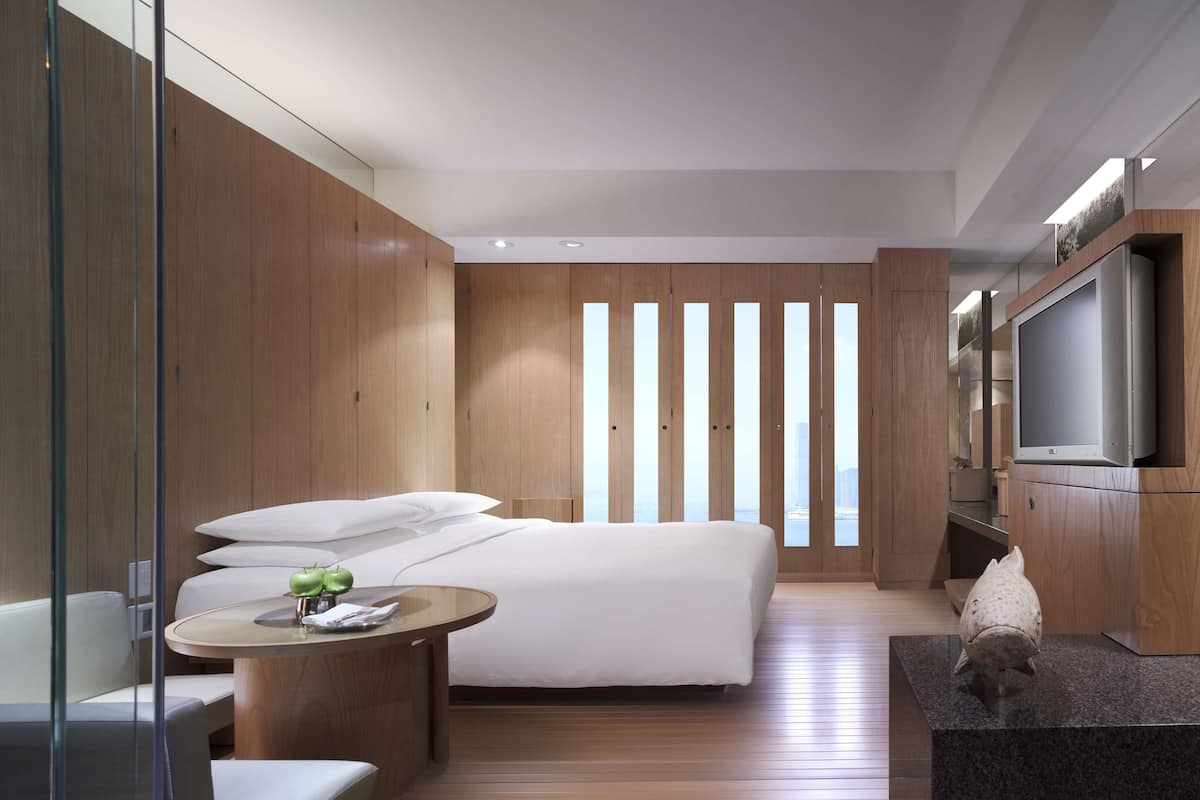 A modern hotel room with a large bed, a TV, a small round table, and a seating area.
