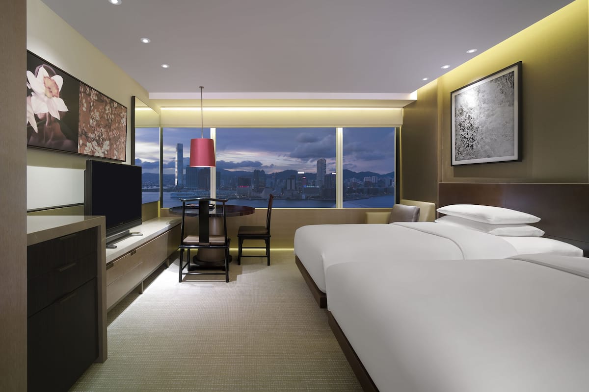 A hotel room with a bed, a desk with a TV, a chair, a table, and a view of a cityscape.